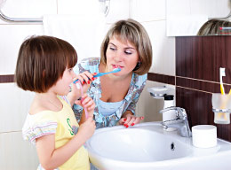 Mother teaching child how to brush her teeth.