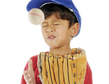 Image of a child wearing a baseball glove with a ball falling toward his face