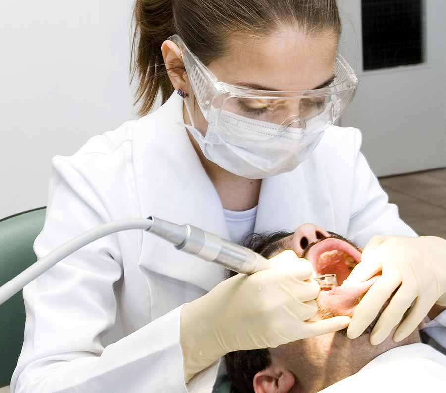 Dentist in a white lab coat conducts an ultrasonic cleaning on a patient.